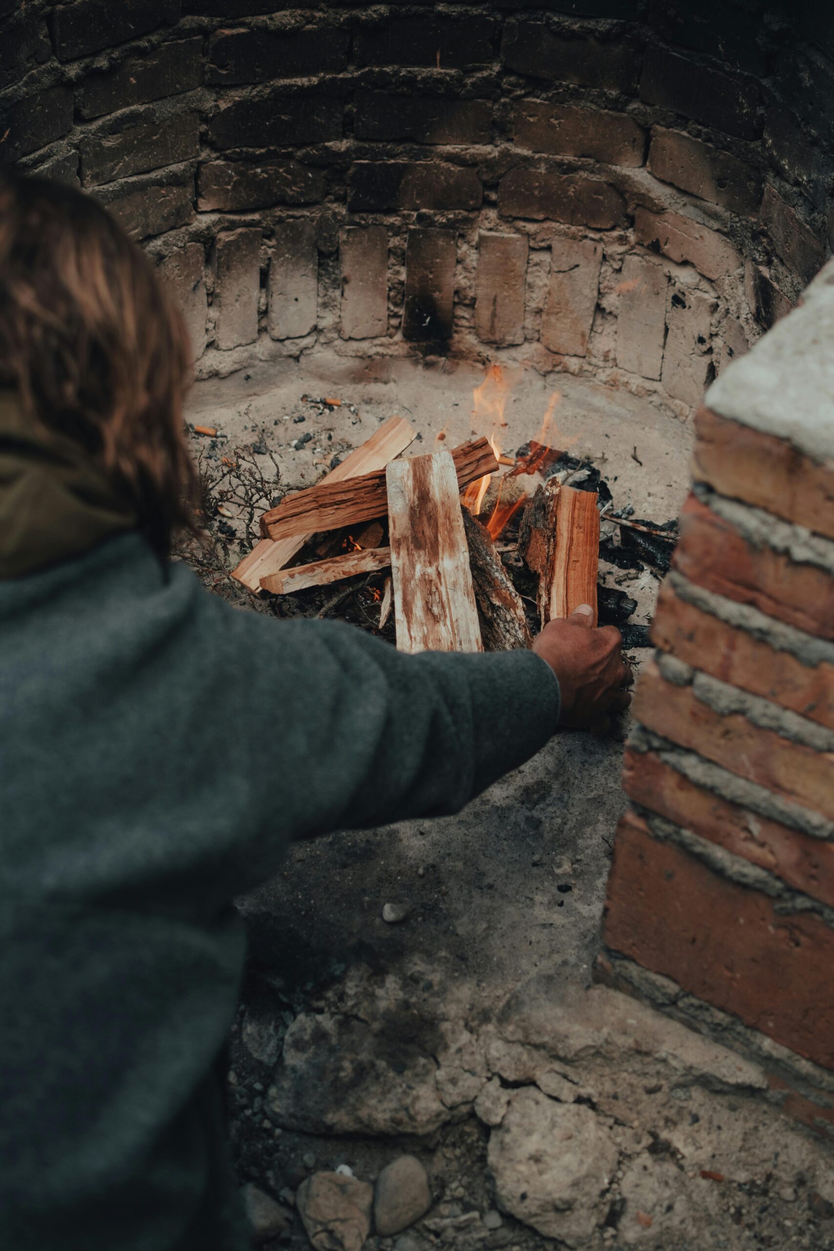A person setting up firewood in a brick fireplace, preparing for a cozy fire.