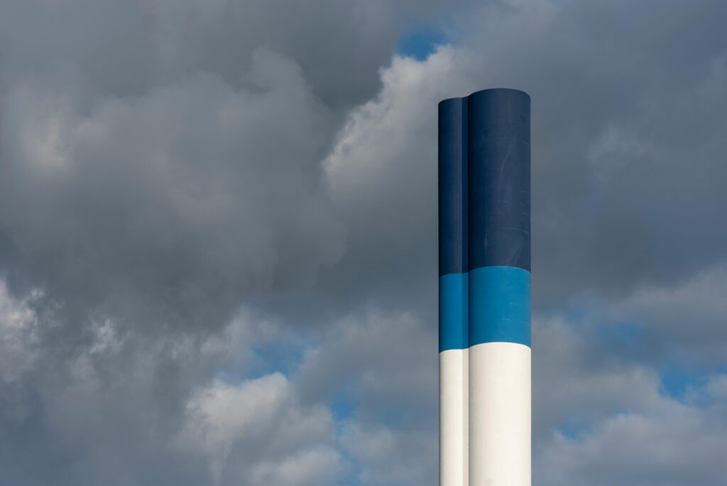 A dynamic industrial chimney with blue and white bands against a cloudy Rotterdam sky, showcasing urban architecture.